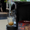 Espresso machine dispensing blend 4 coffee into a glass with Mahalia Coffee capsules nearby.
