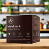 A box of Blend 4 coffee capsules, compatible with Nespresso machines, displayed on a wooden surface with a blurred background of indoor plants and wooden furniture.